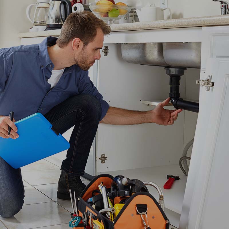 image of man inspecting plumbing under kitchen sink